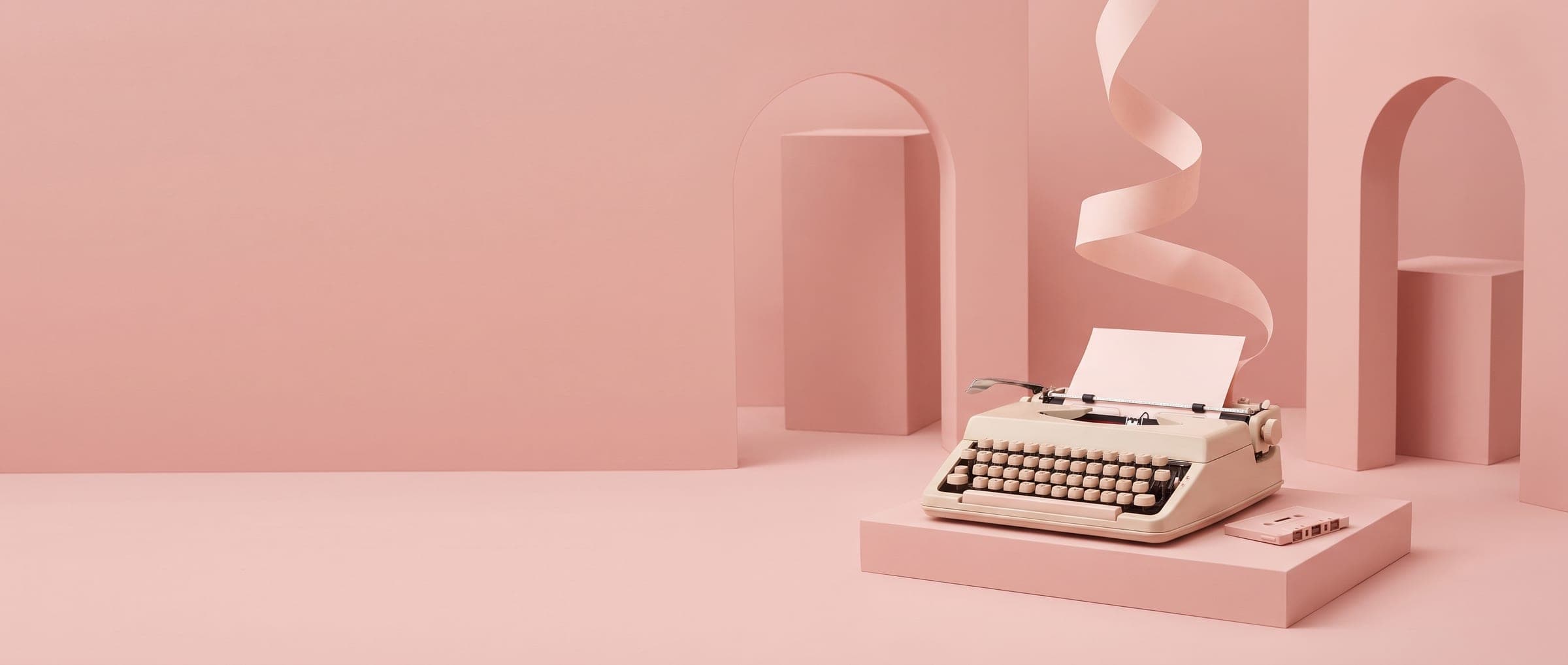 A typewriter on a pink plinth with a ribbon of paper curling up from it