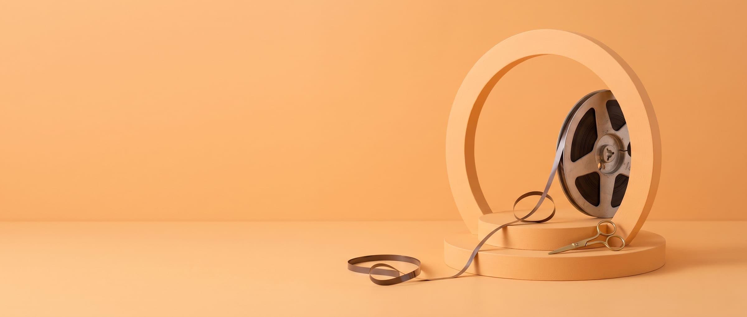 A tape reel inside an orange arch with a strip of tape and a pair of scissors