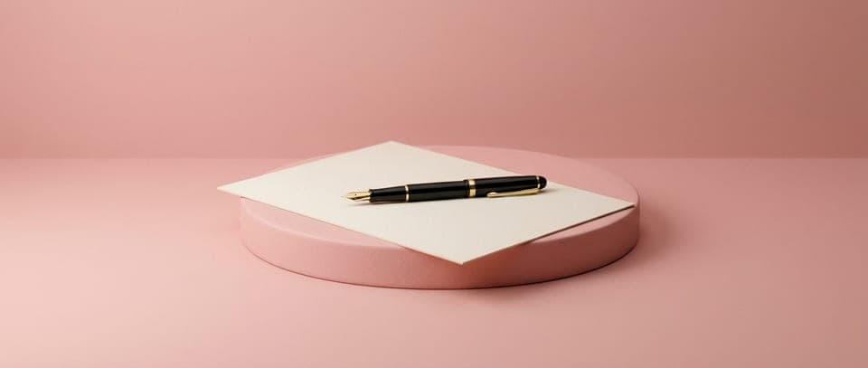 A fountain pen on a blank sheet of paper on a pink plinth