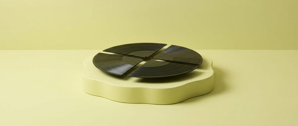 A vinyl record cut into four wedges on a pale yellow plinth