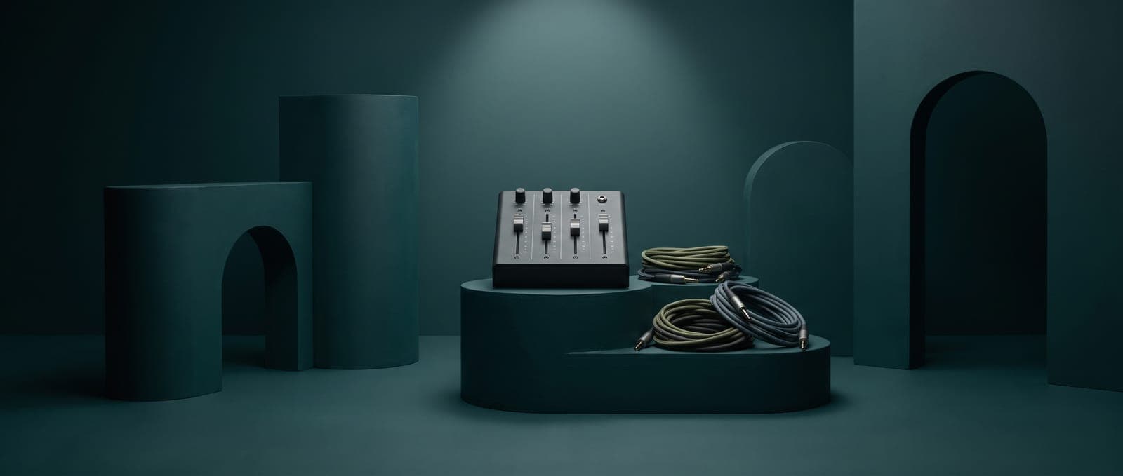 A small mixing desk with four faders and coiled audio cables on a dark green plinth